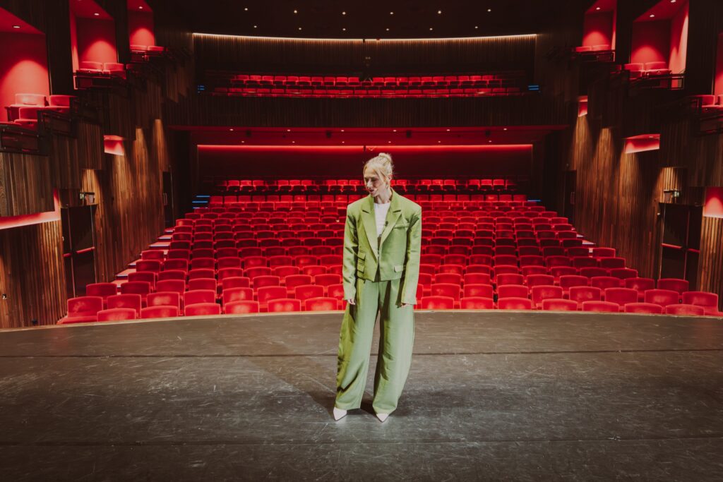 Manouk Schipper staat in groen pak op een theaterpodium
